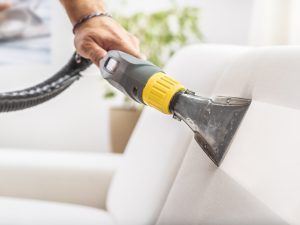 Person using a vacuum cleaner with a yellow grip to clean an upholstered white sofa